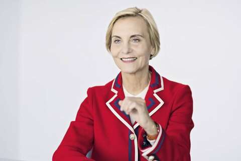 Eine Frau in einem eleganten roten Blazer lächelt und gestikuliert während eines Gesprächs.