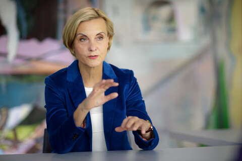 A woman in a blue blazer is gesturing with her hands while speaking at a table.