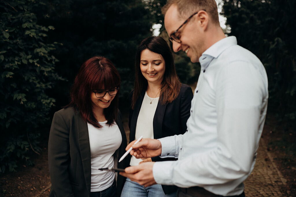 A group of three colleagues, smiling, discuss sustainability ideas outdoors with a tablet.