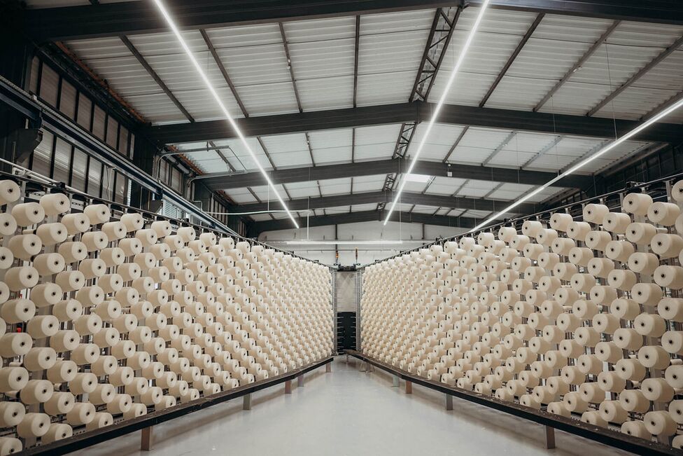Rows of neatly arranged yarn spools fill a large, well-lit textile warehouse, showcasing industrial efficiency.