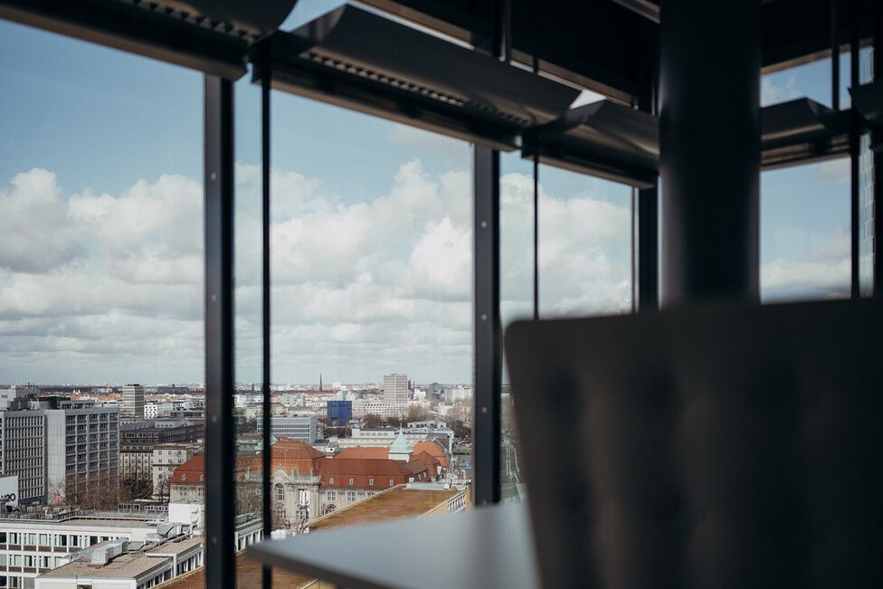 Ein Panoramablick auf die Stadtlandschaft durch große Fenster an einem wolkigen Tag.