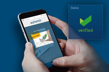 Eine Person hält ein Smartphone mit einer App, die ein Produkt als "authentic" und "verified" bestätigt.