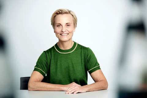 A smiling person in a green shirt sits confidently at a table, exuding a refreshing and positive vibe.
