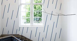Eine Treppe in der Nationalgalerie Berlin mit blauen Streifen an der Wand und einem Ausblick auf grüne Bäume. | © VG Bild-Kunst, Bonn 2023