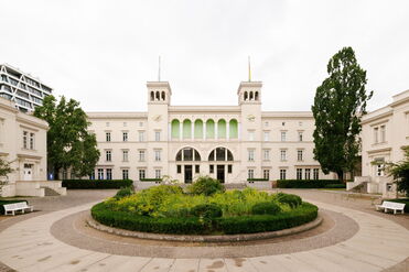 Das historische Gebäude mit Garten und Bäumen zeigt eine elegante Architektur im urbanen Umfeld. (Text KI-generiert)