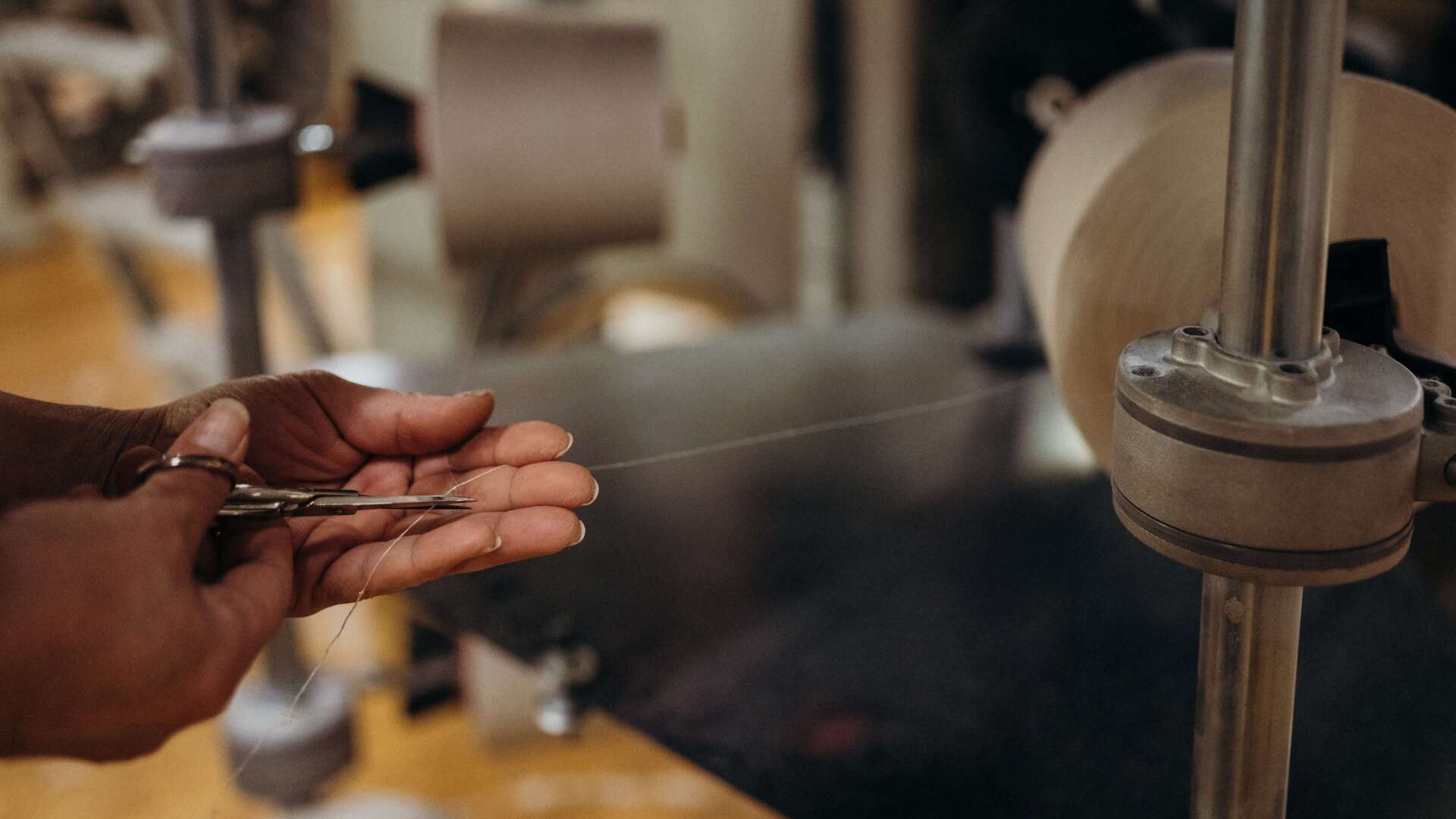 Hands skillfully cut a delicate thread beside a textile machine, highlighting precision in fabric production.
