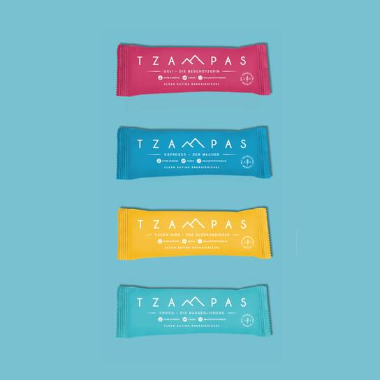 ETHCL Food Labs GmbH - BUSINESS AREAS - Tzampas Four colorful TZAMPAS snack bars are arranged vertically against a blue background, each with distinct packaging design.