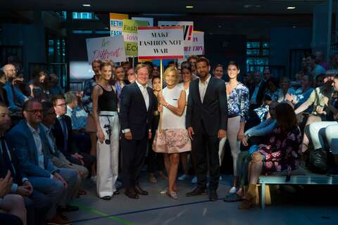 Eine Gruppe von Menschen posiert mit Schildern wie "Make Fashion Not War" auf einem Mode-Event.
