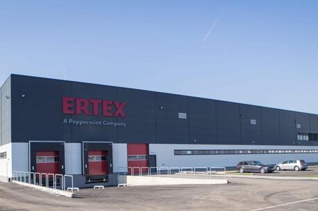 Ein modernes Lagergebäude mit dem Schriftzug "ERTEX" und parkenden Autos bei klarem Himmel.