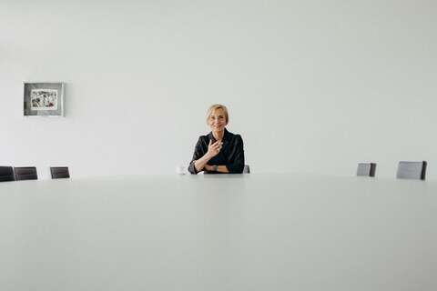 Eine Frau sitzt allein an einem großen Konferenztisch in einem minimalistischen Raum.