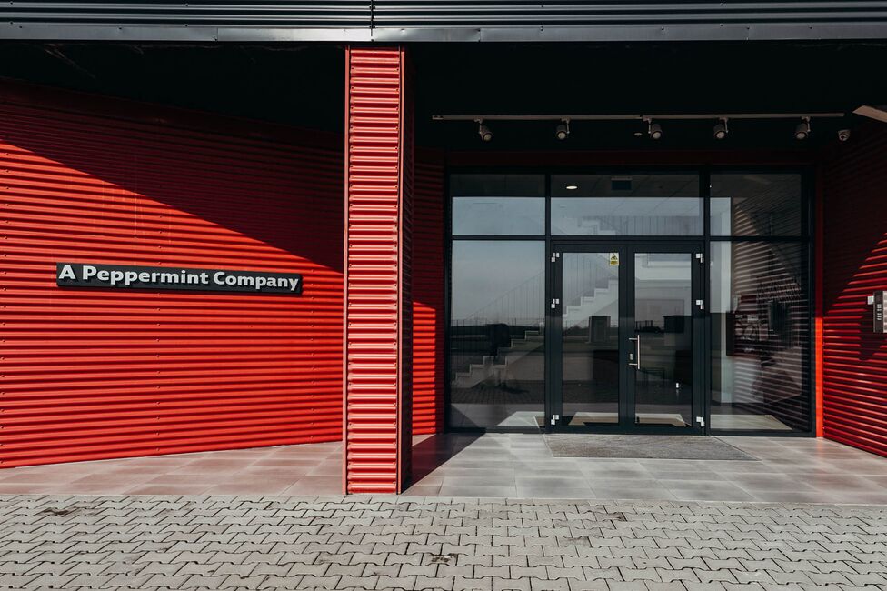 The entrance of a building with a bold red exterior features a sign reading "A Peppermint Company."