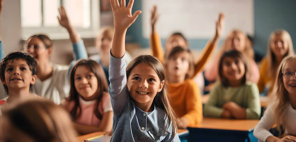 Kinder im Klassenzimmer heben lächelnd die Hände, um sich aktiv am Unterricht zu beteiligen.