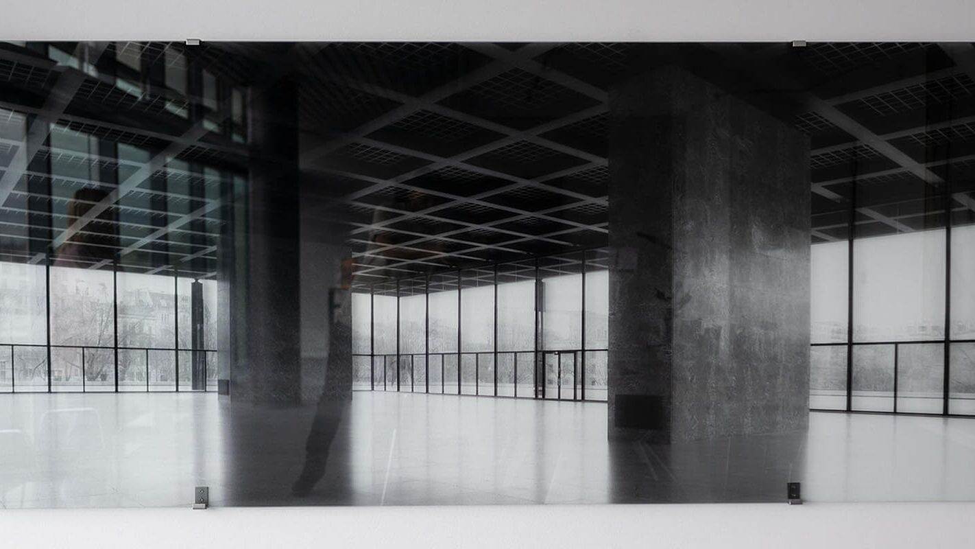 Eine schwarze und weiße Fotografie zeigt einen modernen, leeren Raum mit großen Fenstern und einem reflektierenden Boden.