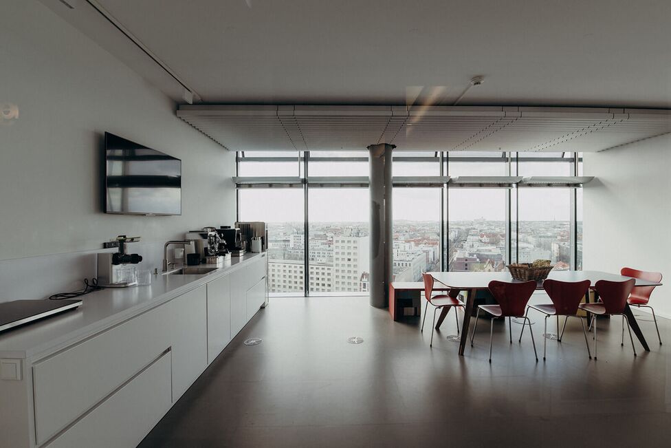 Ein moderner Besprechungsraum mit weißen Wänden, einer Kaffeestation und einem großen Fenster mit Blick auf die Stadt.