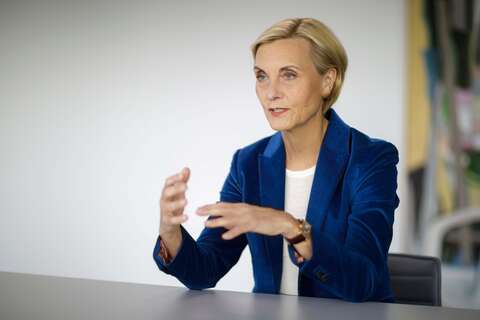 Eine Frau in einem blauen Blazer spricht gestikulierend in einem modernen Büro.