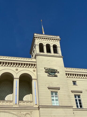 Blick auf den Turm eines historischen Gebäudes mit blauen Himmel und Flagge im Hintergrund. (Text KI-generiert)