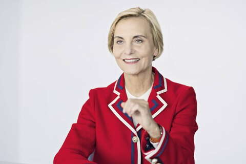 A woman in a vibrant red blazer smiles confidently against a plain background.