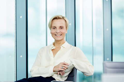 A confident person in a white shirt smiles while seated in a modern office setting, highlighting effective management.