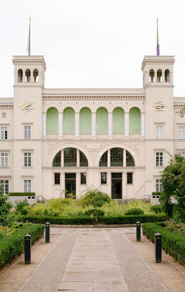 The grand facade of LaForgia features green accents and elegant architecture, framed by lush garden pathways. (Text KI-generiert)
