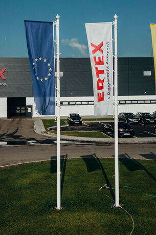 Das Gebäude von Ertex International mit wehenden Flaggen und geparkten Autos davor strahlt Professionalität aus.