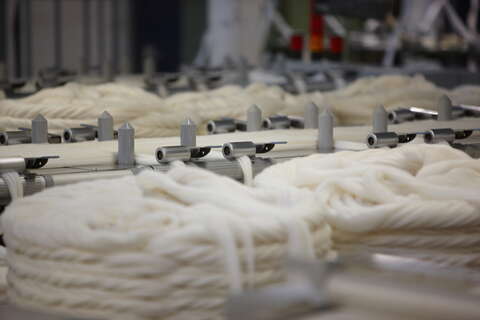 White wool fibers are neatly arranged in large coils on a textile production conveyor, ready for processing.