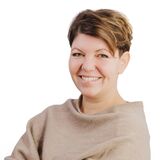 A woman with short hair smiles confidently while crossing her arms, dressed in a cozy sweater against a white background.