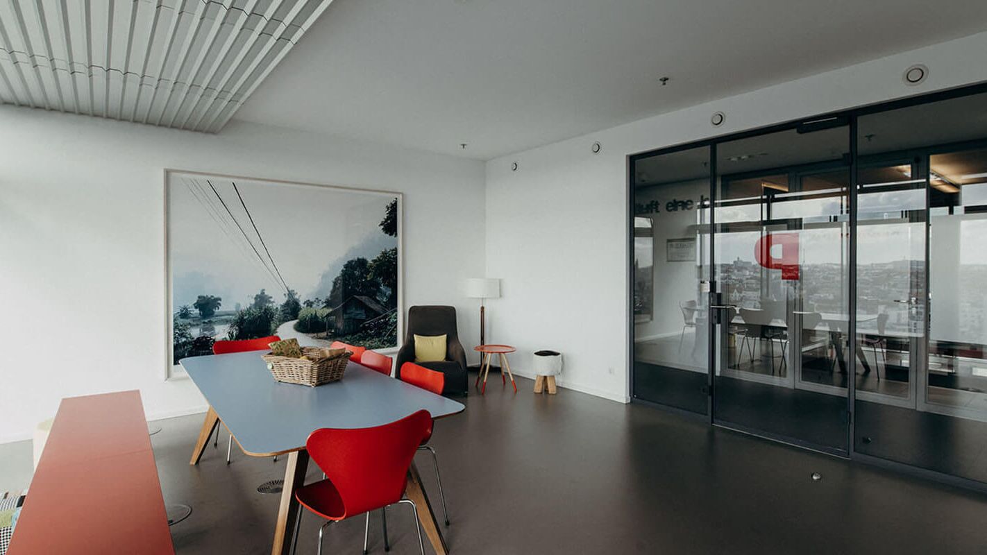 Ein modernes Büro mit einem großen Landschaftsbild, roten Stühlen und einem blauen Tisch schafft eine kreative Atmosphäre.
