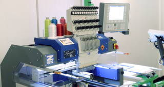 Eine moderne Stickmaschine mit mehreren Garnspulen und digitalem Display stickt ein Design auf Stoff.