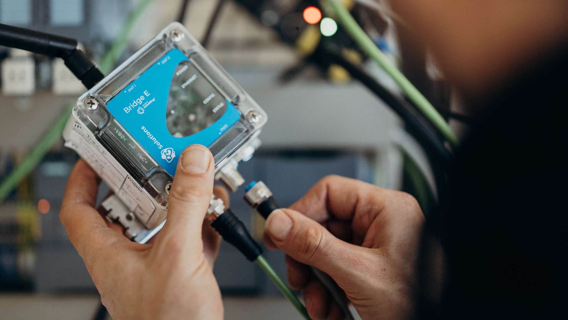 A person is adjusting a Bridge E device, surrounded by cables, focusing on technical connectivity.