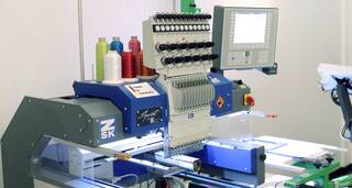 Eine moderne Stickmaschine mit mehreren Garnspulen und digitalem Display stickt ein Design auf Stoff.