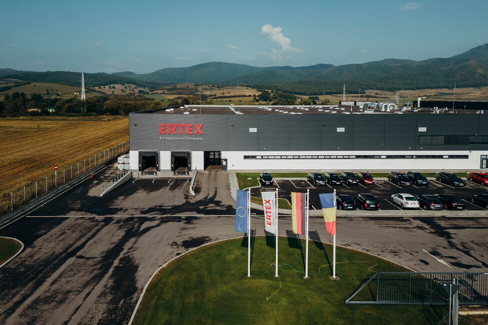 The Ertex International building stands prominently against a backdrop of rolling hills, with flags and parked cars in front.