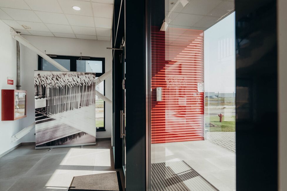 A modern industrial hallway with a striking red door and a large black-and-white photograph on display.