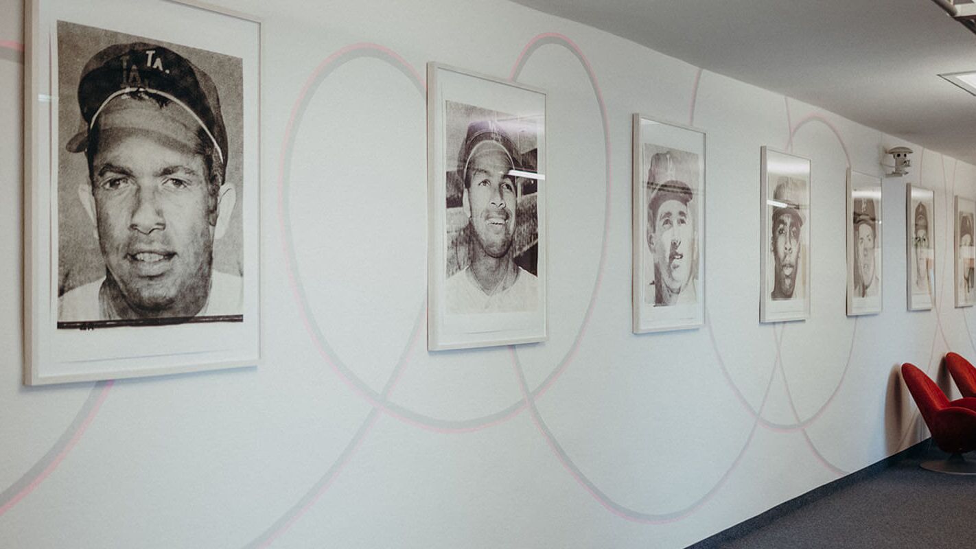 In einem modernen Flur hängen Porträts von Baseballspielern an der Wand, daneben stehen rote Sessel.