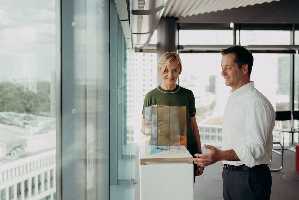 Two people discuss a modern art display in a bright, glass-walled gallery.