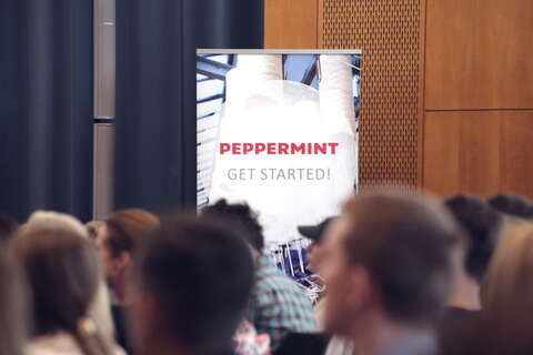 A group of people sits attentively in front of a "Peppermint Get Started" sign at a conference event.