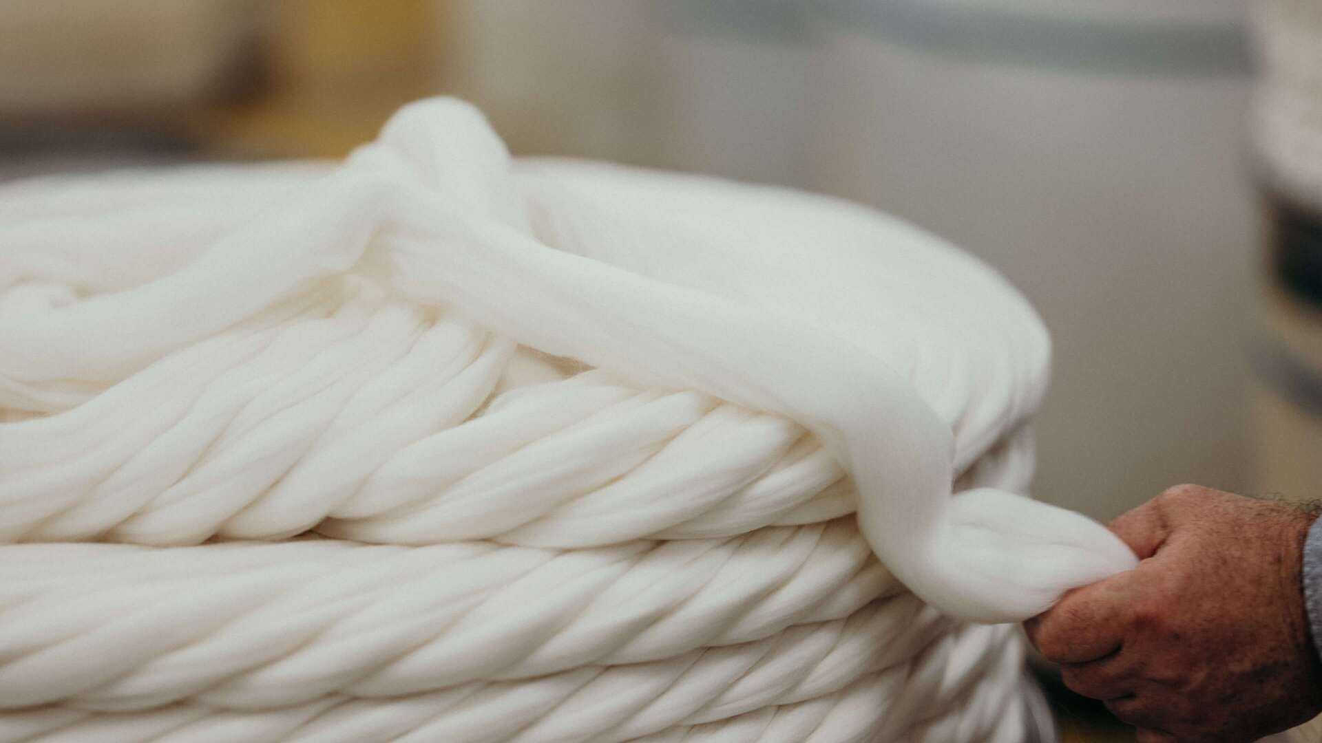 A person holds a thick coil of soft, white wool tightly wound in a factory setting.