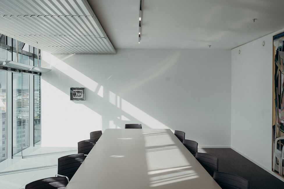 Ein moderner Konferenzraum mit großen Fenstern, durch die Sonnenlicht auf den Tisch und die Stühle fällt.