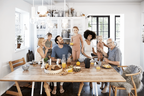 A joyful family gathers around a breakfast table, enjoying food and drinks in a bright, cozy kitchen.