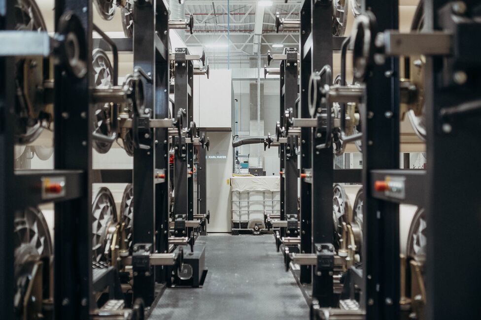 A warehouse aisle is lined with large industrial spools and machinery, highlighting Ertex International's manufacturing setup.