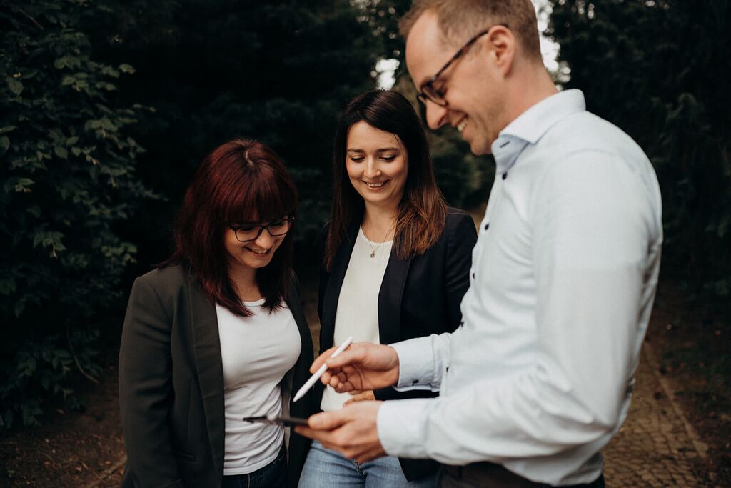 Drei Teammitglieder diskutieren lachend über Nachhaltigkeit, während sie auf ein Tablet schauen.