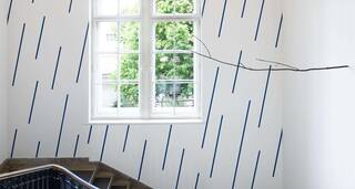 Eine Treppe in der Nationalgalerie Berlin mit blauen Streifen an der Wand und einem Ausblick auf grüne Bäume. | © VG Bild-Kunst, Bonn 2023