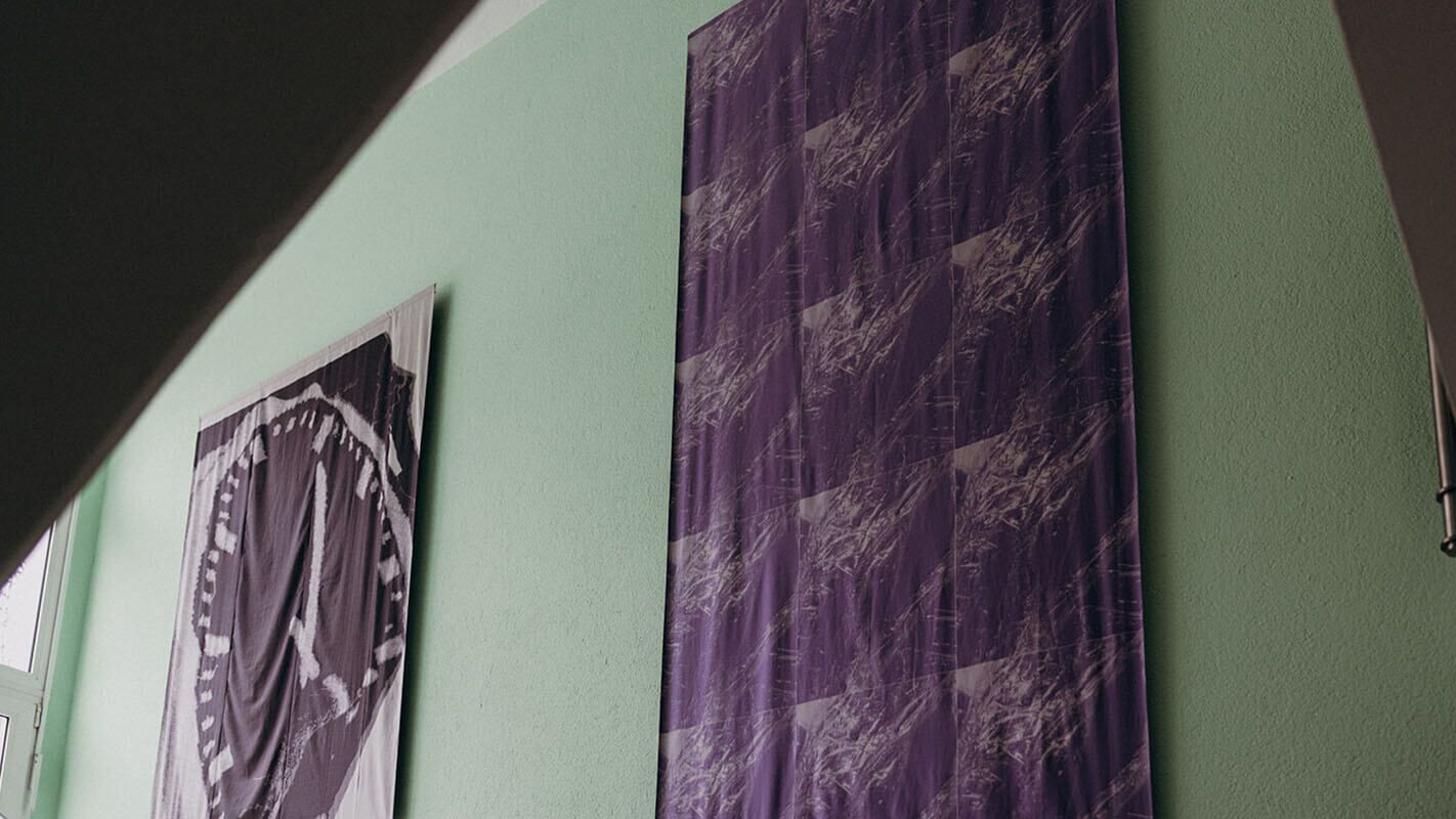 Zwei abstrakte Kunstwerke hängen an einer mintgrünen Wand, eines mit einem violetten Muster und das andere in Schwarz-Weiß.