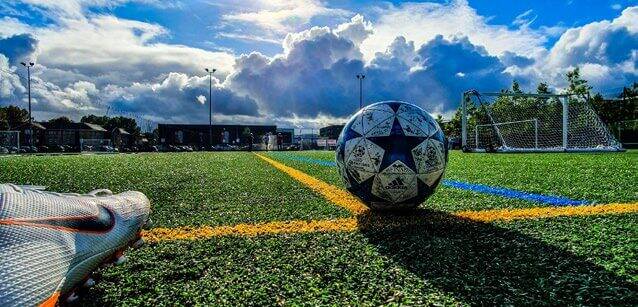 Ein Fußball liegt auf einem sonnigen Sportplatz neben einem Schuh, bereit für soziales Engagement im Spiel.