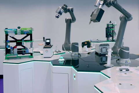 A futuristic lab features collaborative robots and integrated devices working on a hexagonal station.