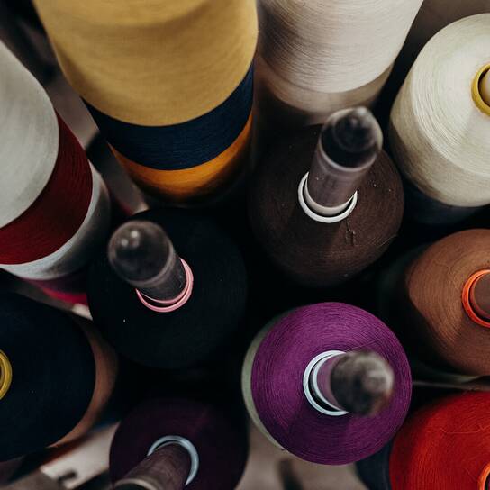 ZKS - BUSINESS AREAS - Specialty Yarns Colorful spools of thread are arranged vertically, showcasing a variety of hues including purple, red, and yellow.