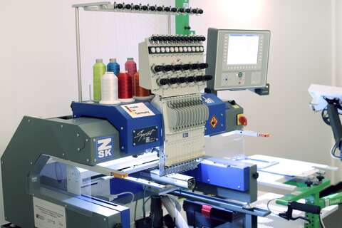 Eine moderne Stickmaschine mit mehreren Garnspulen und digitalem Display stickt ein Design auf Stoff.