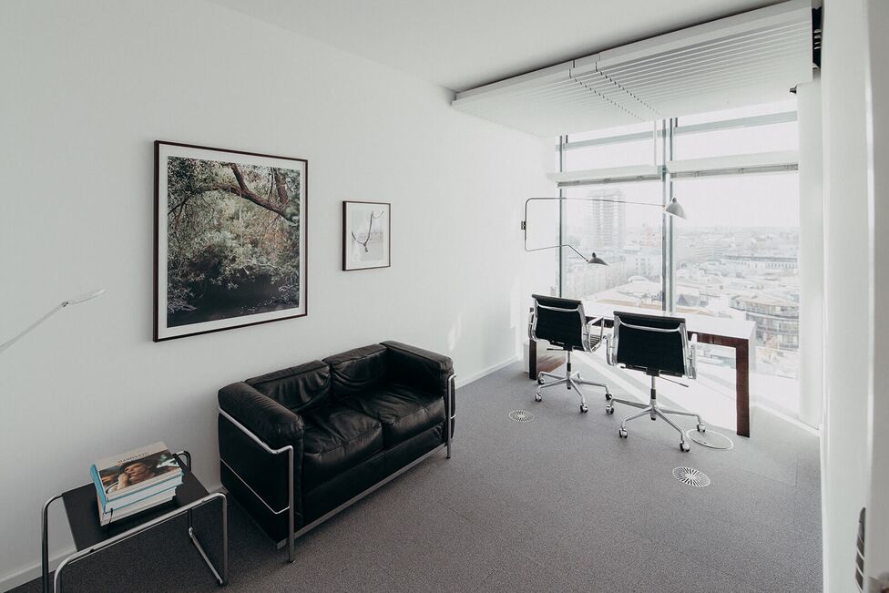 Ein modernes Büro mit schwarzem Sofa, Schreibtisch und Stühlen bietet einen beeindruckenden Ausblick auf die Stadt.