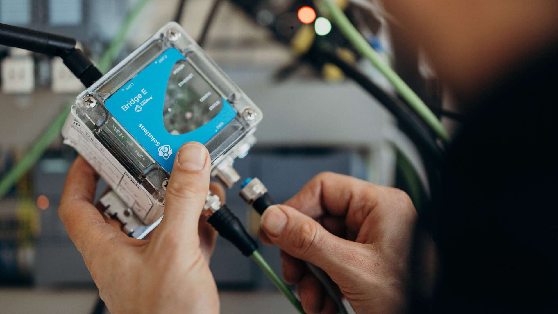 A person is adjusting a Bridge E device, surrounded by cables, focusing on technical connectivity.